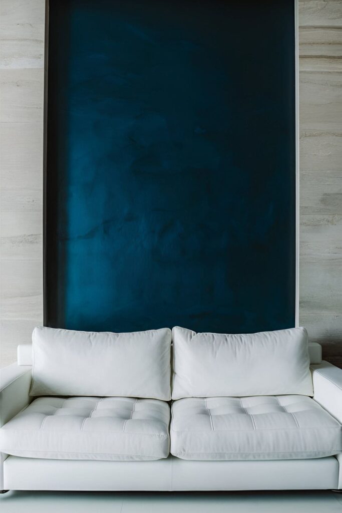 A contemporary living room featuring an accent wall painted in rich, deep blue behind a white couch. The bold color contrasts with the rest of the neutral walls