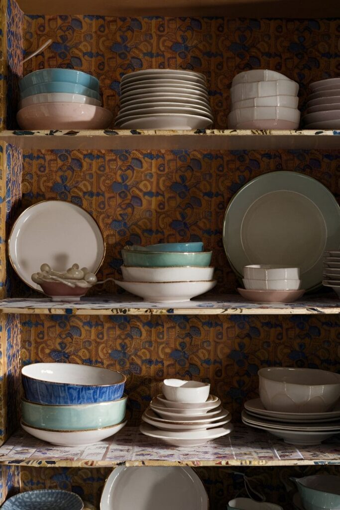 Close-up of a kitchen shelf lined with colorful, patterned cardboard shelf liners, displaying an organized arrangement of plates and bowls