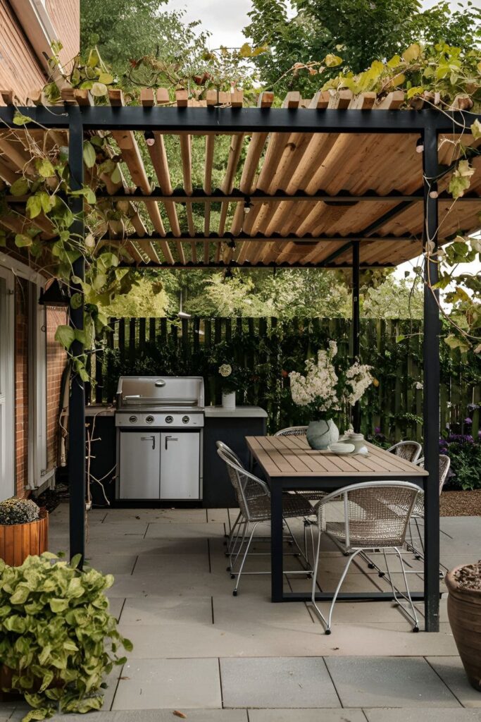 A patio with a wooden pergola for shade, a grill underneath, a dining table and chairs for alfresco meals, decorated with climbing plants and fairy lights