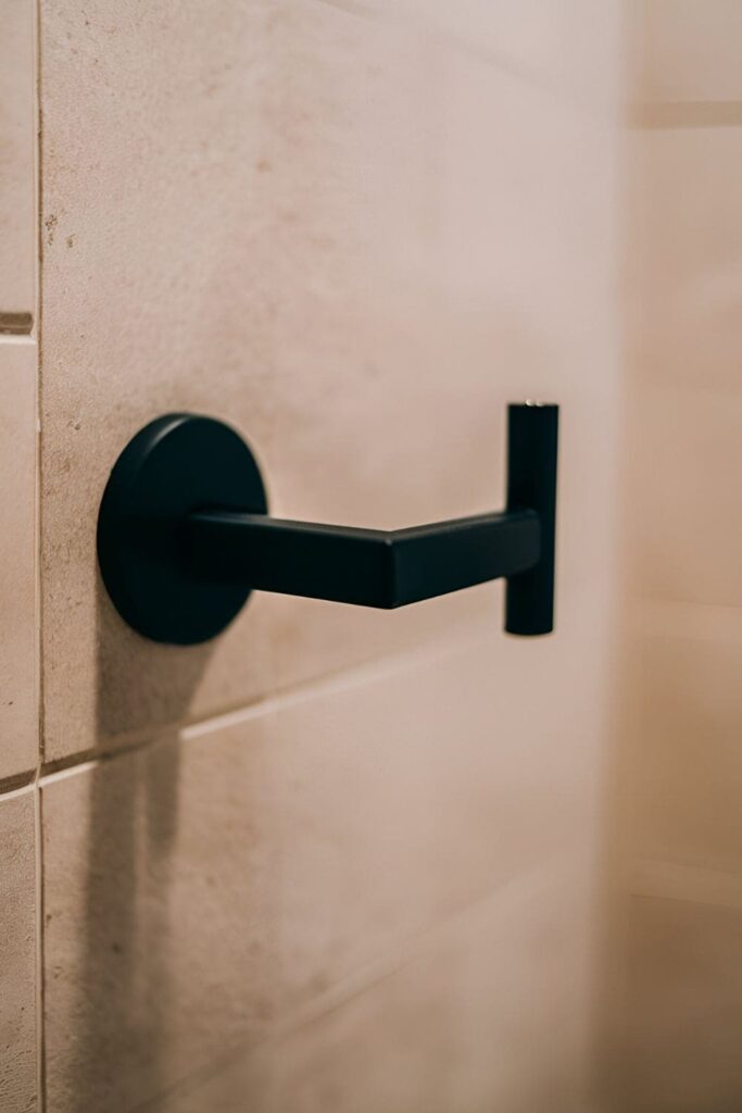 Close-up of a black toilet paper holder mounted on a light-colored bathroom wall, with a sleek and modern design