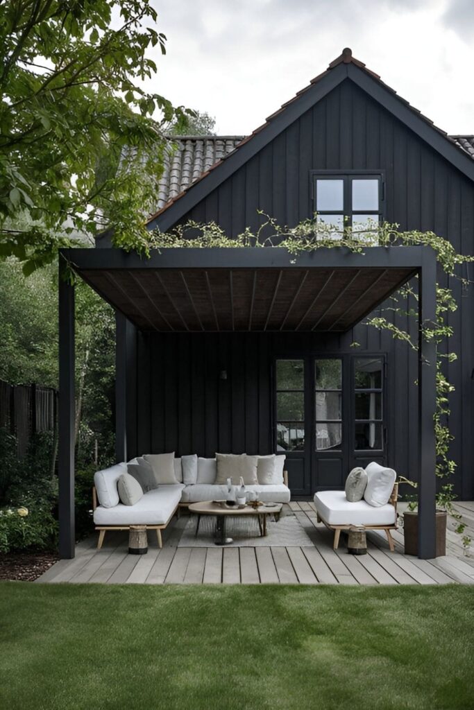 A black house with a shaded pergola creating a cozy, outdoor living space