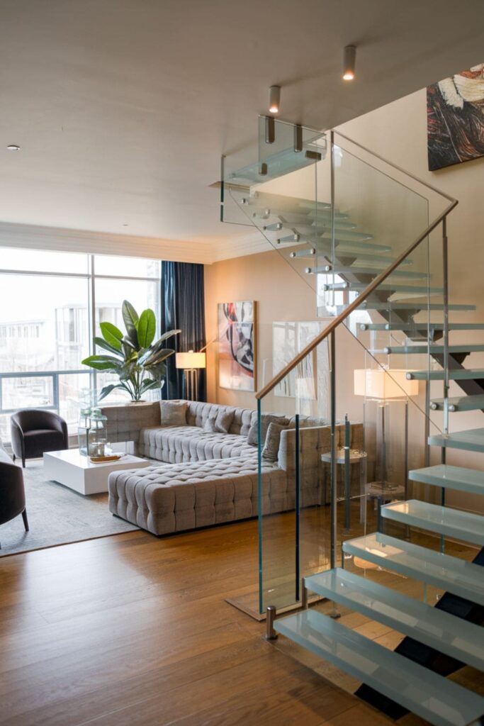 Modern living room showcasing open glass railings on a staircase, allowing natural light to flow through the airy space