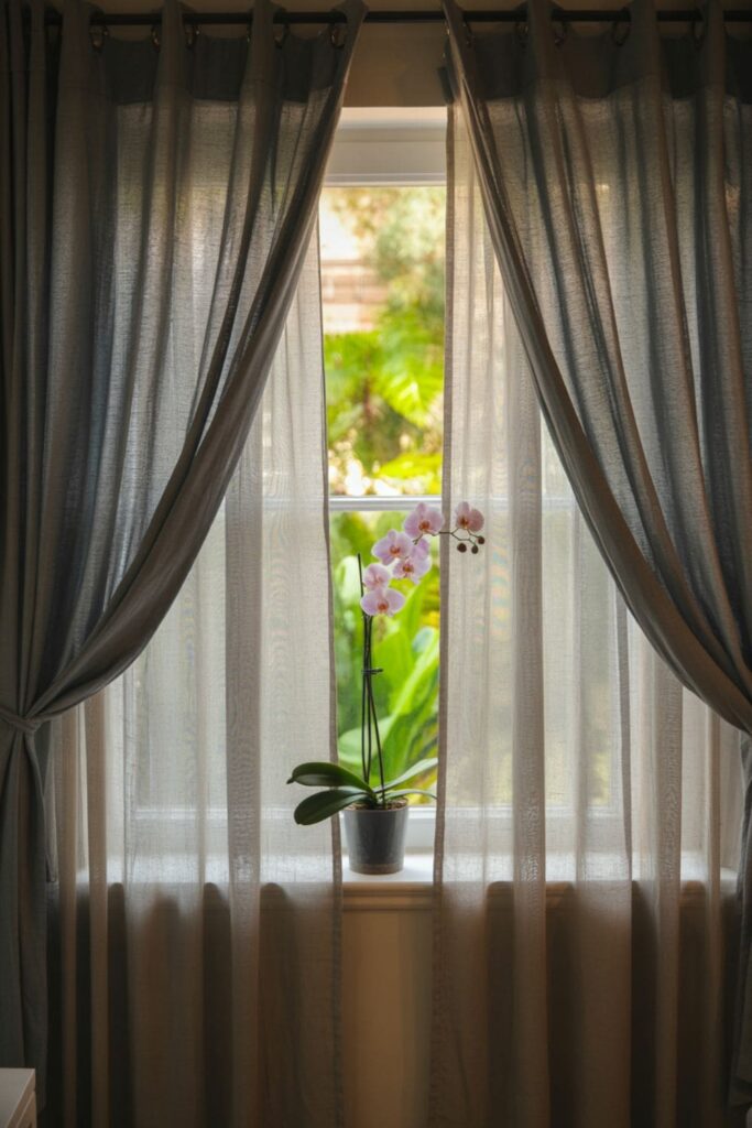 Bedroom window dressed with layered curtains including sheer panels and blackout drapes on the sides