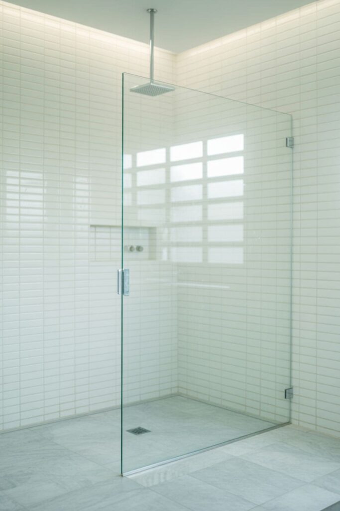 Frameless glass shower partition in a sleek bathroom with stone tile walls